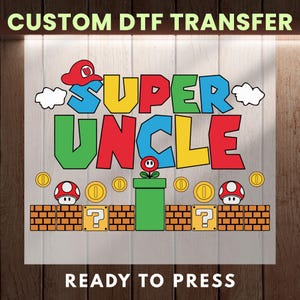 May include: A colorful DTF transfer featuring the text "SUPER UNCLE" in a video game-inspired design. The design includes a red hat, coins, mushrooms, and a green pipe. The words "CUSTOM DTF TRANSFER" and "READY TO PRESS" are also included.