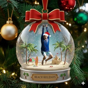 Könnte beinhalten: Ein Weihnachtsornament in Form einer Schneekugel mit einer Strandszene im Inneren, einschließlich Palmen, einer Sandburg und einer Person mit Weihnachtsmütze. Das Ornament hat eine rote Schleife und trägt die Aufschrift "BEACH HOLIDAYS".