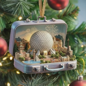 May include: A silver suitcase-shaped Christmas ornament. The ornament opens to reveal a miniature diorama of a theme park with a large geodesic sphere, fireworks, and iconic landmarks. The ornament hangs from a gold ribbon on a Christmas tree.