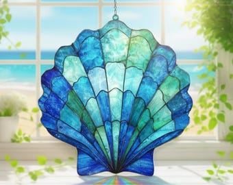 Puede incluir: Un atrapasoles de concha de cristal manchado en tonos azules y verdes cuelga de una cadena. La concha está frente a una ventana con vista al océano y al cielo. El atrapasoles es un artículo decorativo.