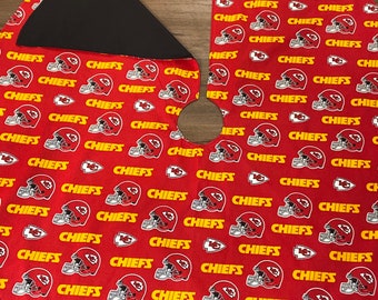 Op de afbeelding: Rode kerstboomrok met een herhalend patroon van Kansas City Chiefs voetbalhelmen en het woord "CHIEFS" in geel. De rok heeft een zwarte achterkant en een cirkelvormige opening voor de boomstam.