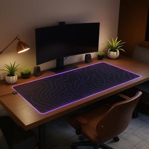 Peut inclure: Un tapis de souris de jeu rectangulaire noir avec une bordure éclairée violette et un motif topographique. Le tapis est sur un bureau en bois avec un écran d'ordinateur, des haut-parleurs et des plantes en pot. Une lampe de bureau est allumée.