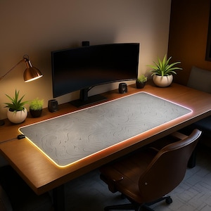Peut inclure: Un grand tapis de souris de jeu rectangulaire gris avec un motif de carte topographique et un bord orange lumineux. Le tapis est posé sur un bureau en bois, avec un écran d'ordinateur, des haut-parleurs et des plantes en arrière-plan. Le bureau est éclairé par une lampe de bureau.