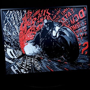 Può includere: Opera d'arte incorniciata con Batman su una moto, resa in nero, bianco e rosso. L'immagine ha uno stile dinamico da fumetto con elementi testuali e un aspetto strutturato. L'opera è ambientata su uno sfondo nero.