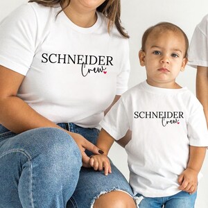 Könnte beinhalten: Drei Personen tragen weiße T-Shirts und blaue Jeans. Die Shirts tragen den schwarzen Aufdruck "SCHNEIDER Crew". Die Person links kniet, die anderen beiden stehen. Der Hintergrund ist schlicht weiß.