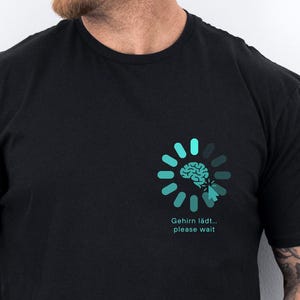 Peut inclure: T-shirt noir avec un motif turquoise représentant un cerveau dans un cercle de chargement. Le texte "Gehirn lädt... please wait" est en dessous. Le t-shirt à manches courtes est en matière souple.