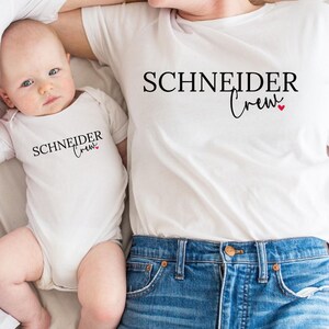 Könnte beinhalten: Eine dreiköpfige Familie trägt passende weiße T-Shirts und einen Body. Die Shirts und der Body tragen den schwarzen Aufdruck "SCHNEIDER Crew" mit einem kleinen roten Herz. Die Erwachsenen tragen blaue Jeans.