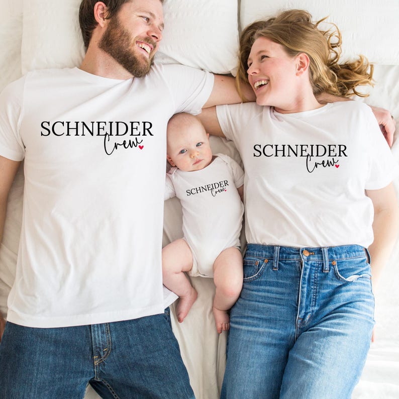 Könnte beinhalten: Eine dreiköpfige Familie trägt passende weiße T-Shirts und einen Body. Die Shirts und der Body tragen den schwarzen Aufdruck "SCHNEIDER Crew" mit einem kleinen roten Herz. Die Erwachsenen tragen blaue Jeans.