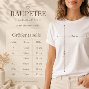 May include: A white Gildan Softstyle T-shirt with the text "RAUPETEE" and a size chart. The chart shows measurements in centimeters for sizes S to 3XL, including width and height. The shirt is being modeled.