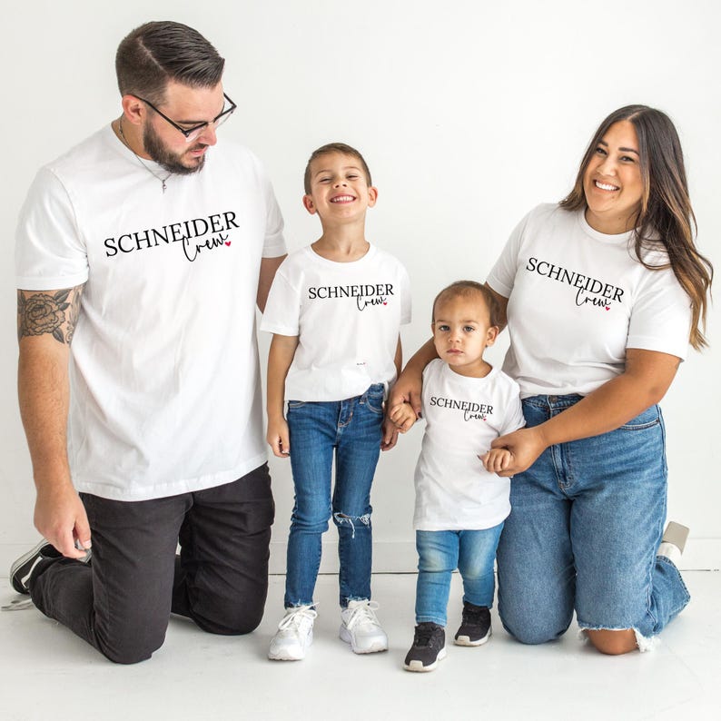 May include: Four people wearing matching white t-shirts with the text "SCHNEIDER Crew" in black script. The shirts are paired with blue jeans and black pants. The family is smiling and posing for a photo.