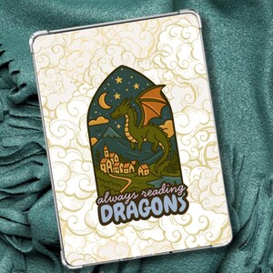 Op de afbeelding: Een rechthoekige tablethoes met een crèmekleurige achtergrond en een herhalend wolkenpatroon. In het midden staat een boogvormige illustratie van een groene draak boven een dorp bij nacht, met de tekst always reading DRAGONS eronder.