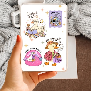Op de afbeelding: Een doorzichtig rechthoekig stickervel met vier eend-illustraties en tekst. De ontwerpen bevatten een eend die leest bij een kaars, een paarse postzegel met Late Night Reader Club, een eend op een roze zitzak en een tas met het opschrift TBR.