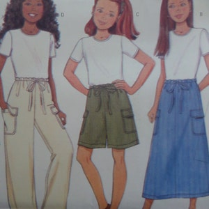 May include: A sewing pattern illustration featuring three variations of outfits consisting of a white short-sleeved t-shirt paired with either cream-colored wide-leg pants, olive green cargo shorts, or a blue cargo skirt, all with drawstring waists.