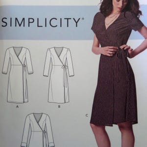 May include: A Simplicity sewing pattern envelope featuring a dark brown wrap dress with a small white geometric print, short sleeves, and a V-neckline. The image includes technical line drawings labeled A, B, and C showing variations of the dress.