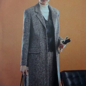 May include: A long, gray, speckled wool-blend coat with notched lapels and flap pockets. Underneath, a white turtleneck sweater is layered with a black zippered vest. The ensemble is paired with a matching gray skirt and black and white gloves.