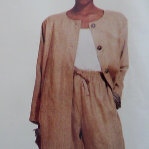 May include: A tan two-piece outfit featuring a long-sleeved, button-down jacket and matching pants. The jacket has a round neckline and the pants have a drawstring waist. The outfit is made of a textured fabric.