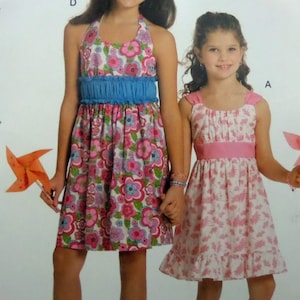 May include: Two girls wearing floral dresses. One dress is a halter style with a blue ruffled waist and a pink and blue floral pattern. The other dress is white with a pink floral pattern and pink straps and waist. Both girls are holding pinwheels.