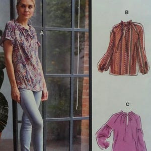 May include: A sewing pattern illustration featuring a short-sleeved paisley blouse labeled A, a long-sleeved patterned blouse labeled B, and a solid-colored long-sleeved blouse labeled C, all with gathered necklines and tie-front closures.
