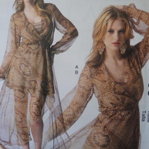 May include: Two women are shown wearing a snakeskin-patterned dress with a sheer overlay. The dress has long sleeves and a V-neckline. The dress is a light brown color with darker brown accents. The model on the right is wearing large earrings.