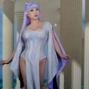 May include: A light blue and silver costume with a reptile-like pattern. The costume has a square neckline and long, flowing sleeves. The model is wearing a lavender wig with cat-like ears.