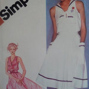 May include: A sewing pattern envelope featuring the text Simplicity. The illustration shows a white sleeveless dress with a sailor collar, dark trim, and two star appliques, alongside a drawing of a pink dress with a V-neck and a belted waist.
