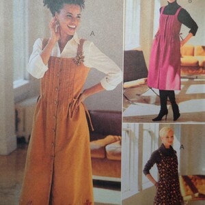 May include: A woman wearing a mustard-colored button-down dress with a white shirt underneath. The dress has a decorative brooch and a tie at the waist. The image also shows two other women wearing similar dresses in different colors and patterns.