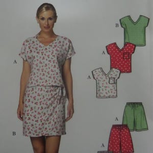 May include: A sewing pattern envelope featuring a V-neck top and wrap skirt in a white fabric with a small red floral print. The illustration includes variations labeled A and B, showing a red polka dot top and shorts, and a green checkered top and shorts.