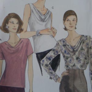 May include: A sewing pattern illustration featuring three tops with cowl necklines. One is a short-sleeved mauve top, one is a sleeveless white top, and one is a long-sleeved top with a blue and grey floral pattern, paired with a dark skirt.