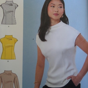 May include: A white sleeveless top with a high mock neck collar and shoulder button details. The image includes technical illustrations labeled A and B, showing the top in a striped pattern, a solid yellow version, and a long-sleeved tan version.