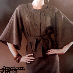 May include: A brown jacket with wide, flared sleeves, a round neckline, and two large buttons at the front. The jacket features vertical pleats radiating from the neckline and a matching fabric tie belt at the waist. The text American Sewing is visible.