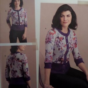 May include: A floral print cardigan with a purple trim and button closure. The three-quarter sleeve sweater features a gray background with a pattern of pink, red, and purple flowers. The cardigan is paired with black pants.