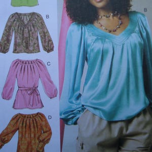 May include: A sewing pattern illustration featuring four blouse designs. Design B is a teal V-neck blouse with long sleeves. Design C is a pink blouse with a gathered neckline and waist tie. Design D is an orange patterned blouse with long sleeves.
