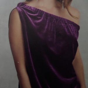 May include: A deep purple velvet top featuring an asymmetrical one-shoulder neckline with a gathered elasticized band. The fabric has a soft, reflective texture characteristic of velvet, creating subtle highlights across the draped surface.