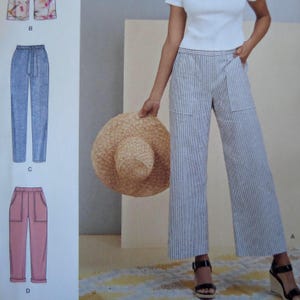 May include: A sewing pattern illustration featuring a white short-sleeve top and blue and white striped wide-leg trousers with large front pockets. The image includes technical drawings of three additional trouser styles labeled B, C, and D.