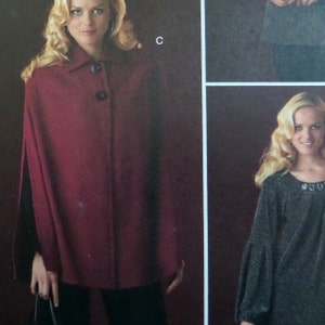 May include: A burgundy cape with a collar and two dark buttons. The cape is worn over a black outfit. The image also shows a woman with blonde hair.