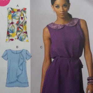 May include: A sewing pattern illustration featuring three garments: a sleeveless top with a white, yellow, and blue floral print and a front ruffle, a light blue short-sleeve top with a side ruffle, and a purple dress with a decorative collar.
