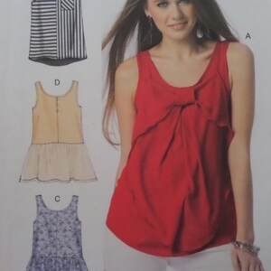 May include: A sewing pattern envelope featuring a red sleeveless tank top with a front bow detail, alongside three illustrated variations: a black and white striped top, a beige top with a peplum hem, and a blue floral print top with a peplum hem.