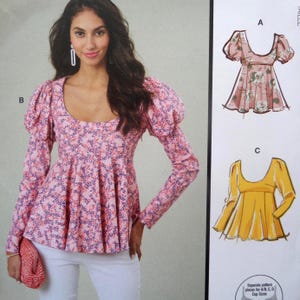 May include: A pink floral print top with long sleeves and a scoop neckline. The top has large, puffed sleeves and a flared peplum. The model is wearing white pants and holding a pink clutch. A pattern illustration is on the right.