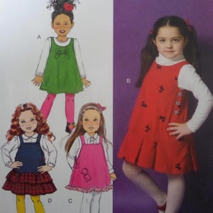 May include: A sewing pattern illustration featuring four variations of a sleeveless jumper dress worn over a long-sleeved white shirt. The designs include a green dress with a bow, a red dress with small black motifs, a pink dress, and a plaid skirt.