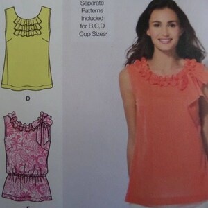 May include: A sewing pattern illustration featuring a sleeveless top with a ruffled neckline. The image displays a yellow top, a pink floral print top with a gathered waist and bow, and an orange top with a ruffled collar and side bow. Text reads: Separate Patterns Included for B, C, D Cup Sizes.