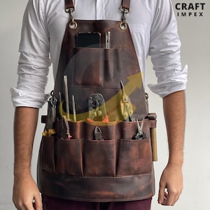 May include: A brown leather apron with multiple pockets, holding various tools. The apron has adjustable straps and metal hardware. The apron is worn over a white shirt and burgundy pants. The Craft Impex logo is visible in the upper right corner.