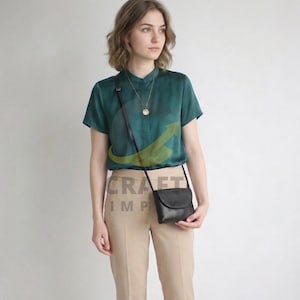 Könnte beinhalten: Eine Frau trägt eine dunkelgrüne kurzärmlige Bluse und eine beige Hose, mit einer schwarzen Umhängetasche. Eine goldene Halskette ist sichtbar. Der Text "CRAFT IMP" ist sichtbar.