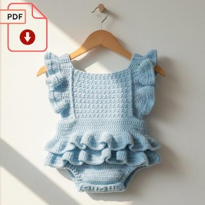 Op de afbeelding: Een lichtblauwe gehaakte romper met ruches en fladdermouwen, hangend aan een houten hanger. Het kledingstuk is handgemaakt en lijkt voor een baby of peuter te zijn. Een PDF-pictogram met een downloadpijl staat linksboven.