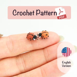 May include: Two miniature crochet ladybugs, with orange and black bodies, are shown. The ladybugs are on a person's hand. The image includes text that reads "Crochet Pattern PDF" and "English Version".