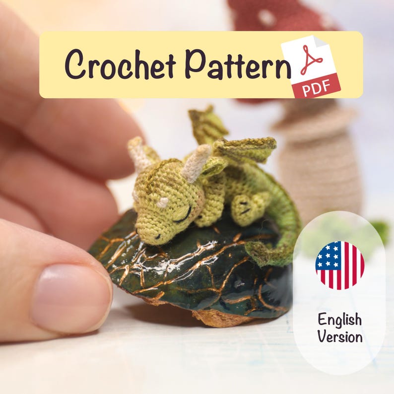 Tiny green micro crochet dragon sleeping on a polished dark stone, handmade amigurumi miniature with small horns and wings, held between fingers to show scale, fantasy crochet creature pattern preview.
