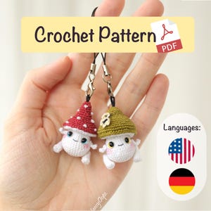 Peut inclure: Deux breloques en forme de champignon au crochet, l'une avec un chapeau rouge à pois blancs et l'autre avec un chapeau vert. Les breloques ont des visages souriants et sont attachées à des cordons noirs avec des fermoirs argentés. Le texte "Crochet Pattern PDF" est inclus.