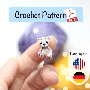 Könnte beinhalten: Ein winziger, gehäkelter Teddybär in Grau- und Rosatönen wird gezeigt. Der Bär hat schwarze Augen und eine kleine, dunkle Nase. Das Bild enthält den Text "Crochet Pattern PDF".