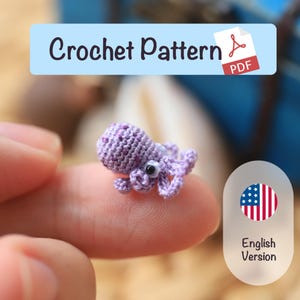 Könnte beinhalten: Ein winziger, handgehäkelter Oktopus in Lilatönen, der auf einer Fingerspitze ruht. Der Oktopus hat detaillierte Tentakel und einen strukturierten Körper. Das Bild enthält den Text "Crochet Pattern PDF" und "English Version".