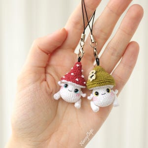 Pu&ograve; includere: Due ciondoli a forma di fungo all'uncinetto con facce sorridenti e cordini neri. Un fungo ha un cappello rosso a pois bianchi, l'altro un cappello verde. I ciondoli sono bianchi con guance rosa e piccole braccia e gambe.