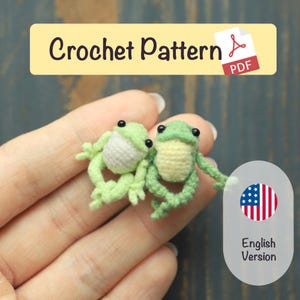 Può includere: Due piccole figurine di rana all'uncinetto in verde chiaro e bianco sono tenute in una mano. Le rane hanno occhi neri e sono collegate. L'immagine include il testo "Crochet Pattern PDF" e "English Version".